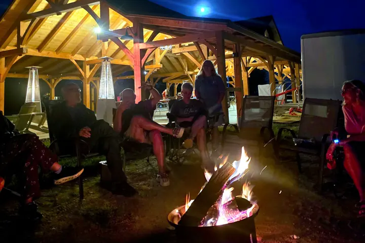 Guests gathered around a fire pit at night beside the lit pavilion